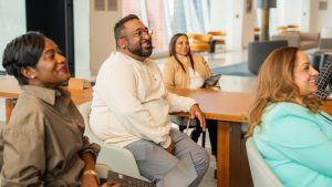 Learning Opportunities A group of colleagues wearing lanyards listen to a speaker during a learning session at an office.