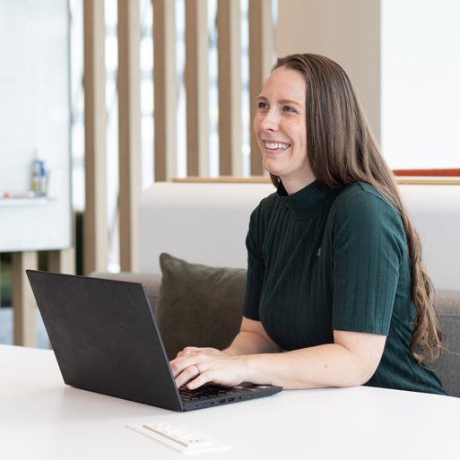 Une collègue vêtue d’une blouse verte sourit dans une réunion.