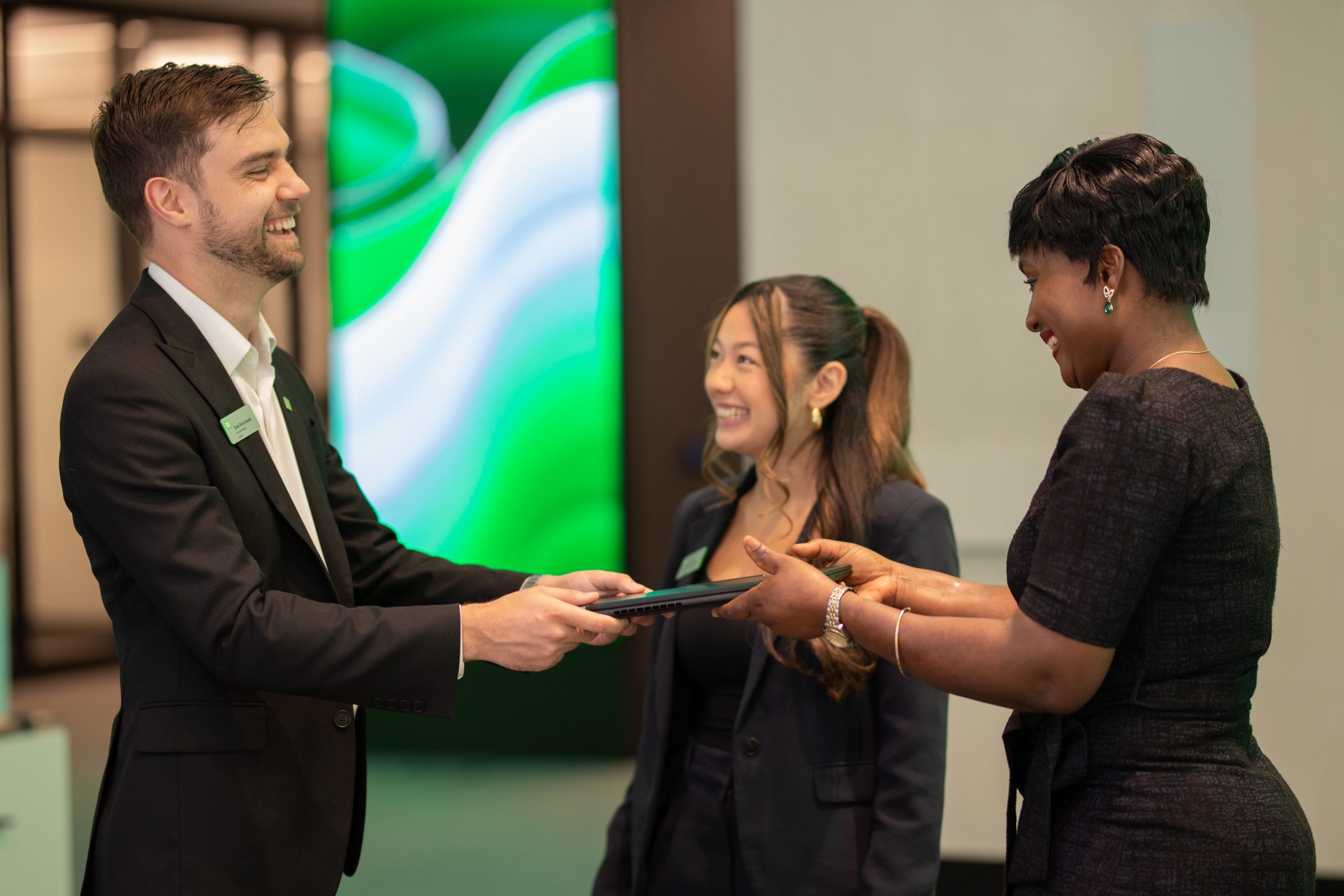Une collègue sourit et regarde la caméra pendant qu’elle est assise à côté d’une personne qui tape sur un ordinateur portable.