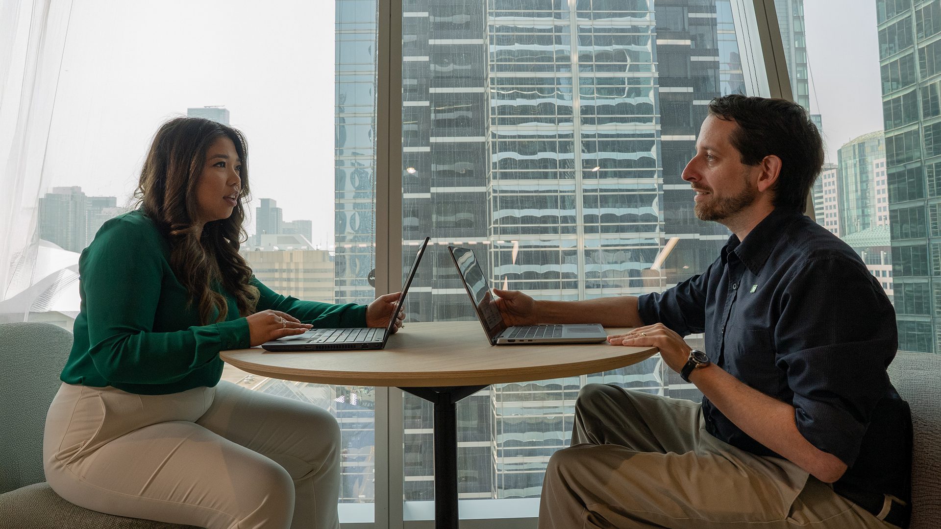 Two colleagues look at a tablet while walking together in an office hallway.