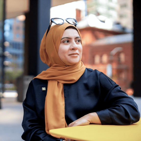 A TD colleague wearing a hijab and a green TD pin sits out front of a TD office.
