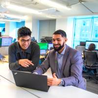 Deux collègues sourient en regardant un écran d’ordinateur.