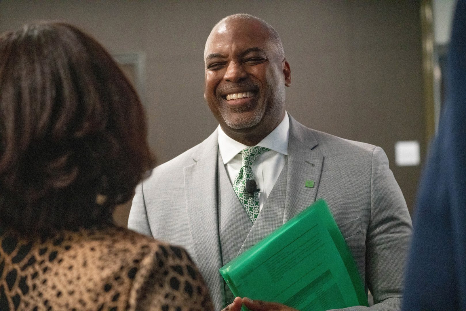 A colleague with a green tie and TD lapel pin holds a green folder while speaking to a customer.