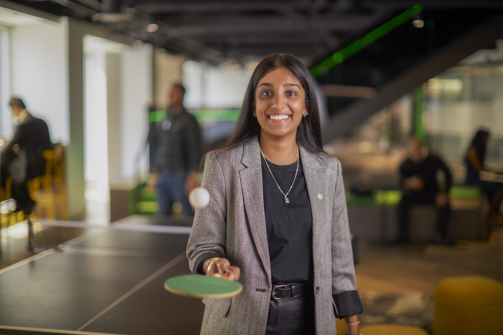 A TD colleague wearing a green TD lapel pin bounces a ball on a ping pong paddle.