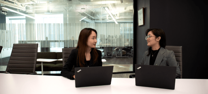Two colleagues have a discussion while seated in front of their laptops.