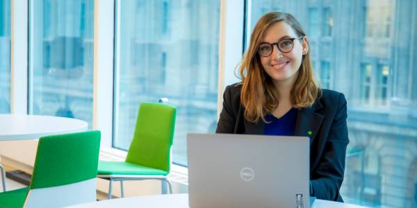 A new colleague smiles while working on a laptop in an open concept office area.