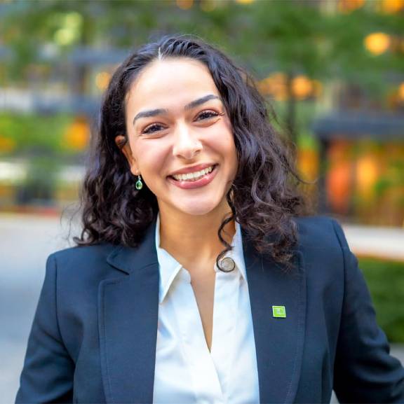 A colleague wearing a blazer with a green TD pin smiles in front of TD head office.