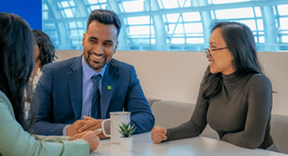 Three colleagues chat around a cafeteria lunch table.