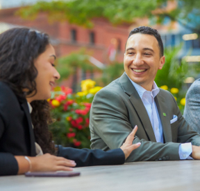Trois collègues souriants sont assis à une table de pique-nique à l’extérieur.